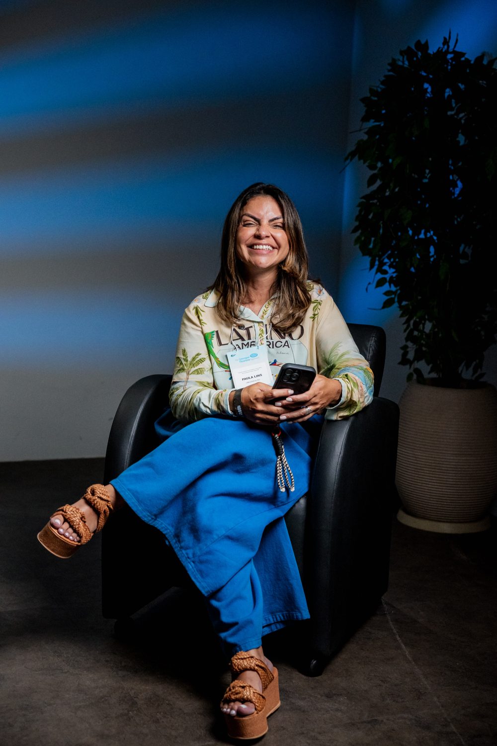 Paula Lins sorrindo, sentada em uma poltrona